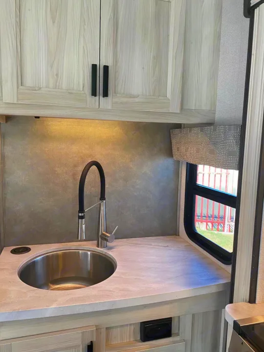 Modern RV rental kitchen featuring a sleek sink, dark faucet, light wood cabinets, and bright under-cabinet lighting.. Forest River Sunseeker 2022