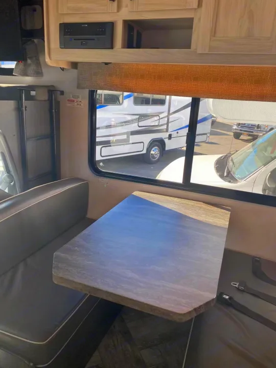 RV rental interior with a dinette, table, booth seats, window view of other campers, and an entertainment system.. Forest River Sunseeker 2022