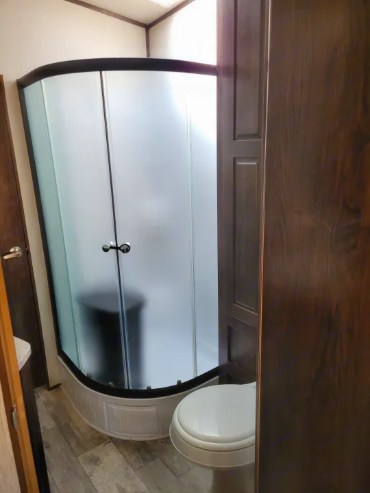 RV rental bathroom: curved frosted shower, toilet, and wooden cabinetry. A compact, functional RV interior.. Heartland Fuel 305 2018