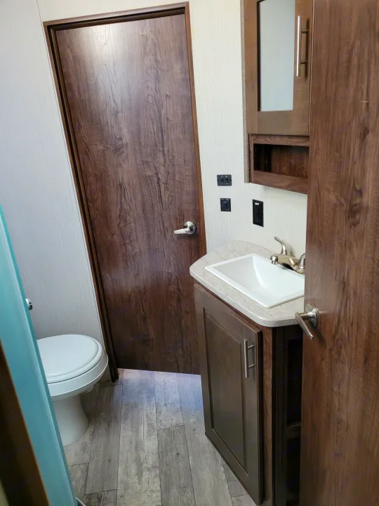 Modern RV rental bathroom interior featuring a dark wood door, toilet, sink vanity, and mirrored cabinet.. Heartland Fuel 305 2018