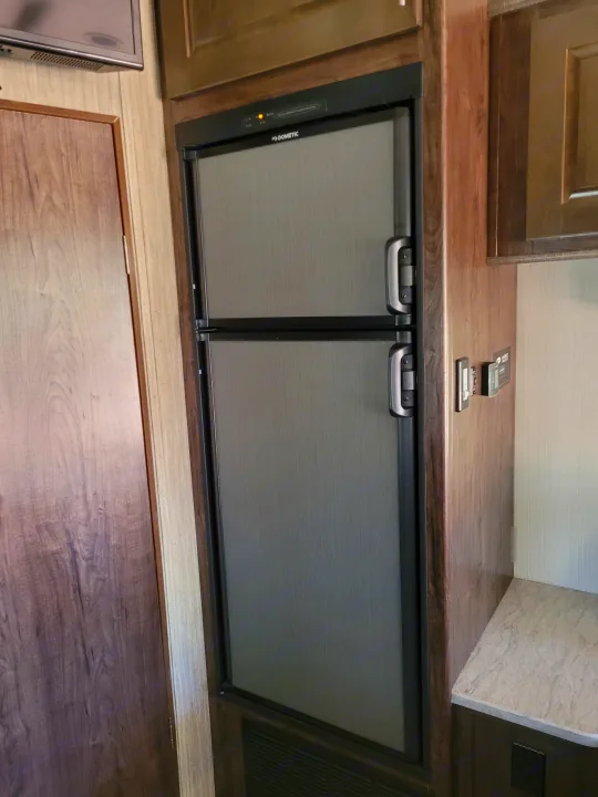 This rv rental features a Dometic two-door refrigerator within wood-grain cabinetry. Controls are visible to the right.. Heartland Fuel 305 2018