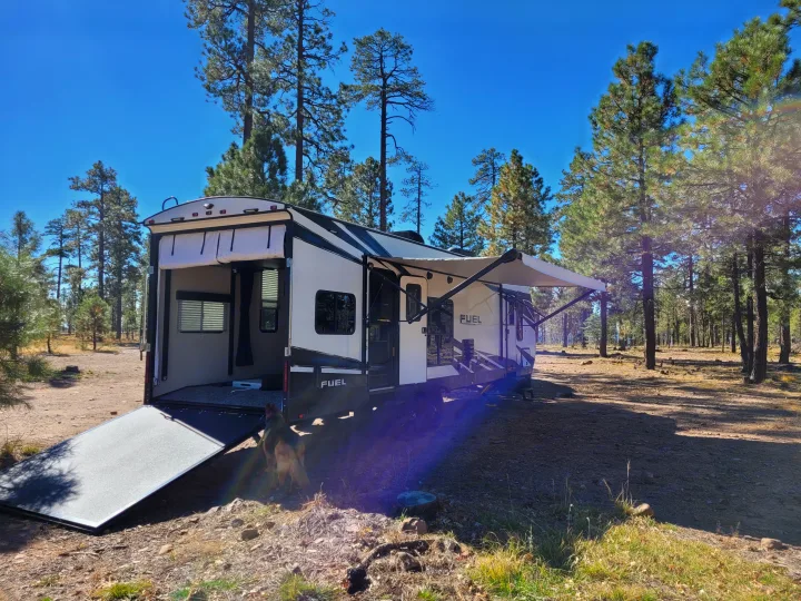 Fuel toy hauler RV rental parked in a sunny pine forest with its back ramp down, awning extended. A dog is nearby.. Heartland Fuel 305 2018