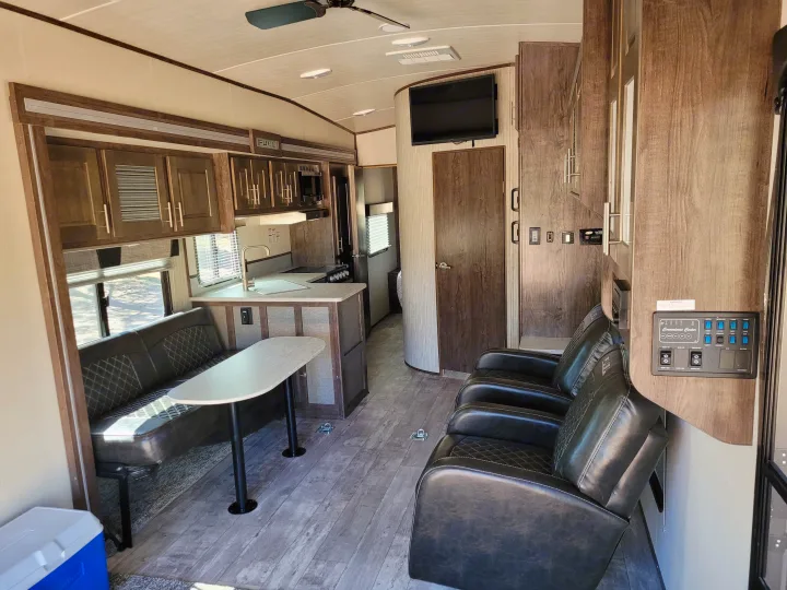 Spacious rv rental interior showing a kitchen, dining booth, and three recliners with wood-look flooring.. Heartland Fuel 305 2018