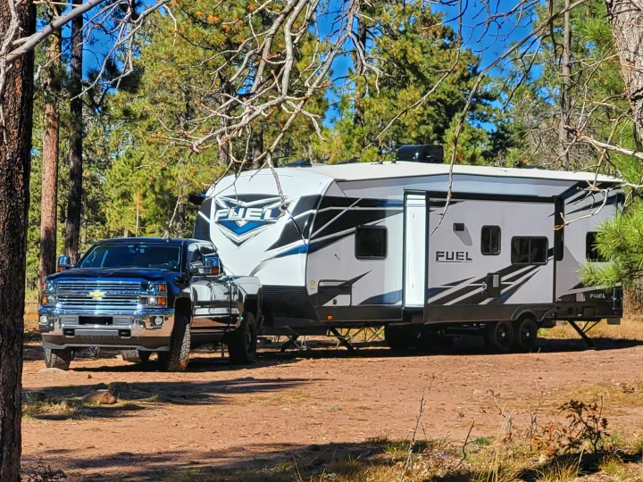 This "FUEL" toy hauler RV rental, hitched to a truck, is set up in a sunny, forested campsite, ready for adventure.. Heartland Fuel 305 2018