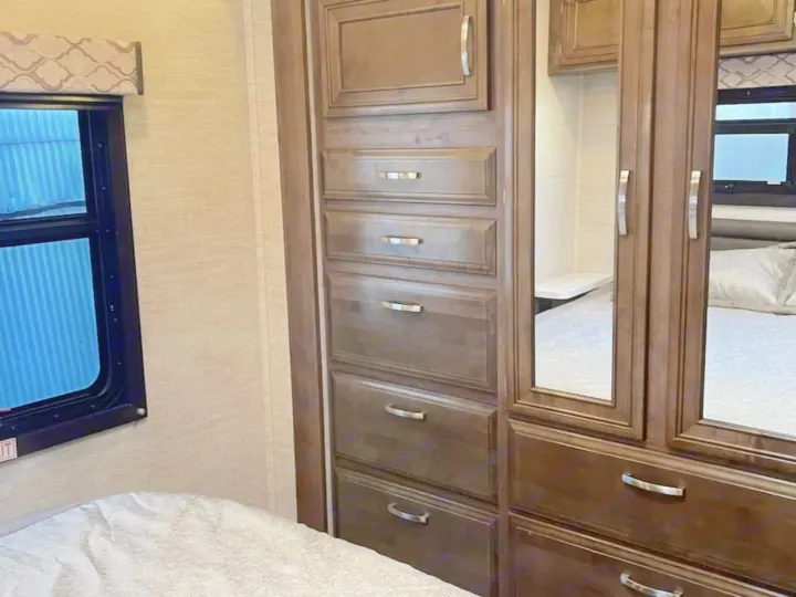 Spacious RV rental bedroom with dark wood cabinets, mirrored wardrobe, and large window over the bed.. Ford Ford 2022