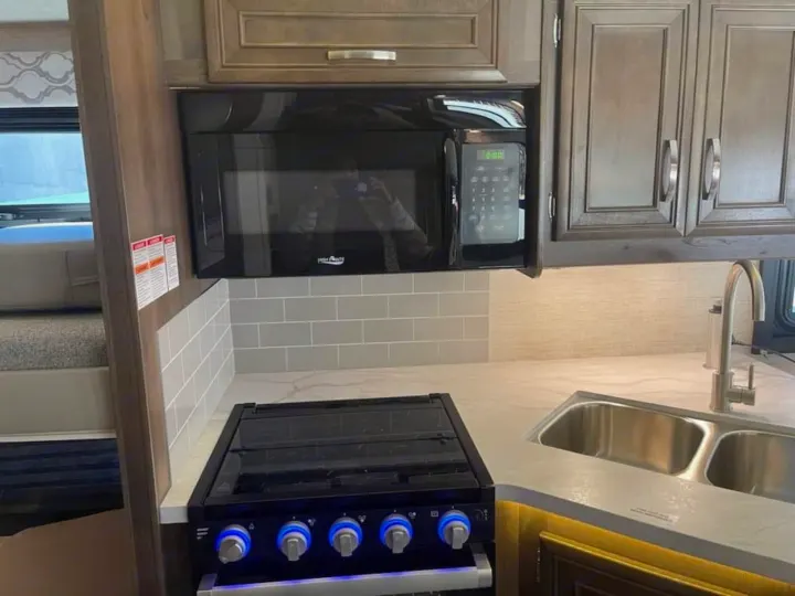 This modern RV rental kitchen features an over-the-range microwave, stove with blue glowing knobs, and a double sink.. Ford Ford 2022