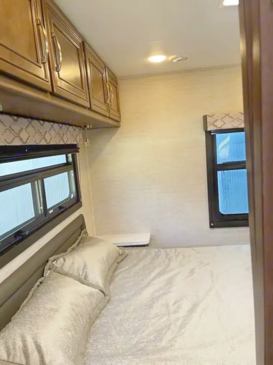 This RV rental bedroom features a comfortable bed with neutral bedding, windows, and convenient overhead cabinets.. Ford Ford 2022