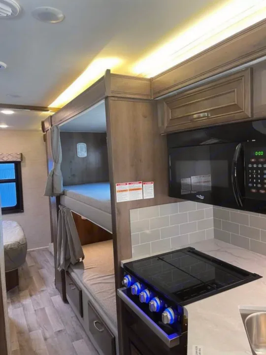 Modern RV rental interior: kitchen with microwave, stovetop, sink & subway tile, plus cozy bunk beds.. Ford Ford 2022