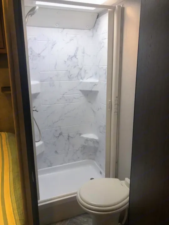 An RV rental's compact bathroom, showing a white, marble-patterned shower with built-in shelves and a toilet.. Forest River Other 2021