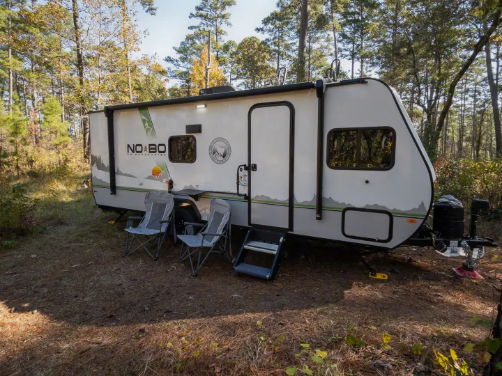 Adventure awaits! This RV rental travel trailer is set up in a serene forest campsite with outdoor chairs.. Forest River NOBO 19.7 2022