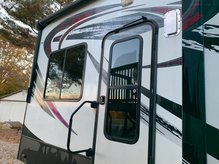 Side of an RV rental with vibrant red, black, and purple graphics. Features an entry door with window, adjacent window, and grab handle.. Heartland Cyclone 2015