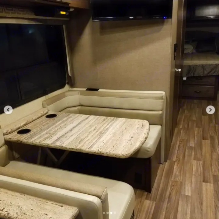 Modern RV rental interior with a dinette, table & TV. Cozy bench seating & wood-look floor lead to the rear bedroom.. Thor A.C.E. 2018