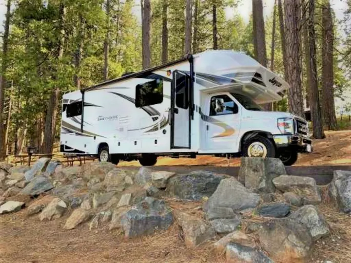 A white Jayco Greyhawk **RV rental** parked at an elevated campsite with rocks and tall pine trees, ready for adventure.. Jayco Greyhawk prestige 30XP 2020