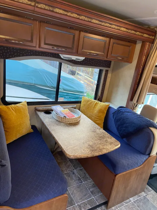 Comfortable RV rental dinette with blue seating, yellow pillows, a dining table, and a view of a boat outside.. Thor Freedom Elite 2013