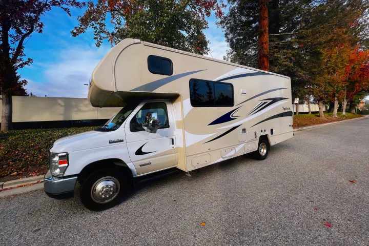 Beige & white Class C RV rental, a Spirit model, parked on a street; perfect for road trips.. Winnebago Spirit 2020
