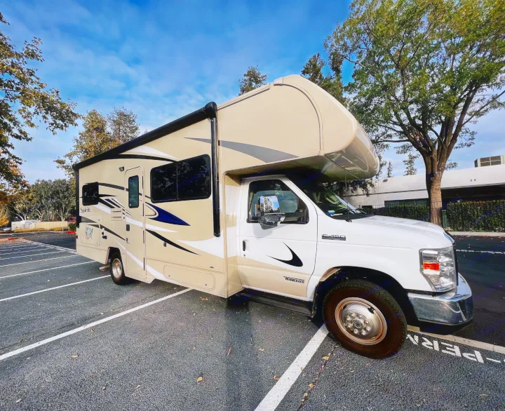 This cream/tan Winnebago Spirit Class C RV rental (Ford E-450) is parked in a lot, ready for adventure.. Winnebago Spirit 2020