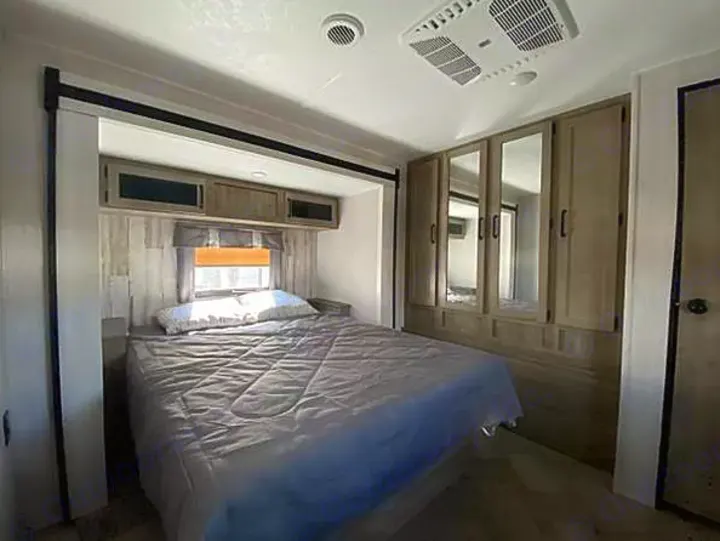 RV rental bedroom: a cozy space with a bed, overhead cabinets, mirrored wardrobe, and AC, ready for your comfortable travels.. Palomino Puma 31-RLQS 2022