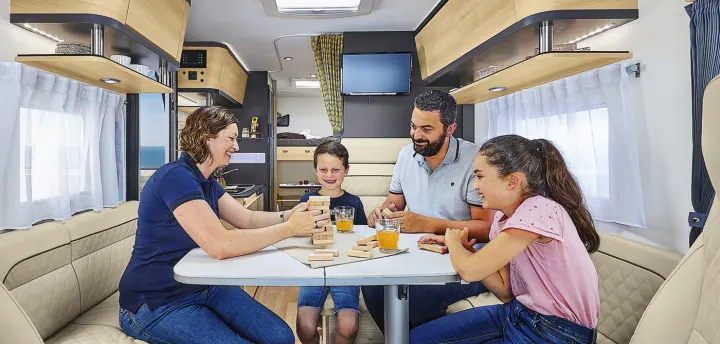 A family enjoys playing Jenga together inside a comfortable RV rental, offering a scenic ocean view.. ITINEO CS660 2022