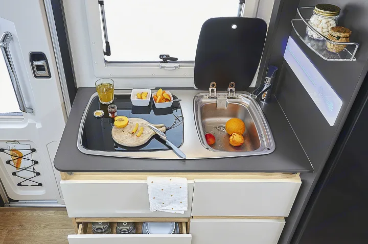 A fully equipped compact kitchen in an rv rental, showing a sink, cooktop, and fresh fruit for a meal.. ITINEO CS660 2022