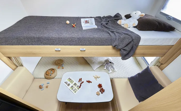 RV rental interior: A top bunk bed with gray bedding and stuffed animals, above a lower play/seating area with a table & toys.. ITINEO CS660 2022