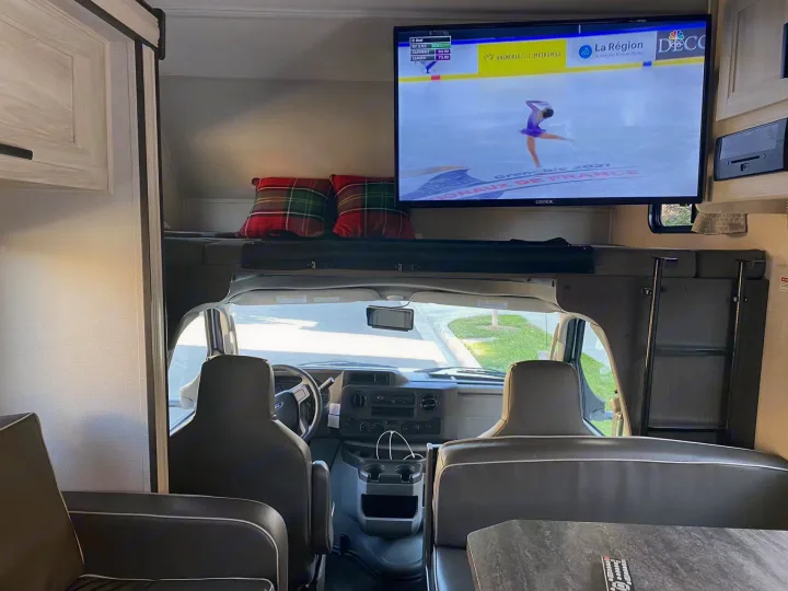 Cozy RV rental interior with TV showing figure skating, overhead bunk, and cockpit. Ready for adventure!. Forest River Sunseeker 2022