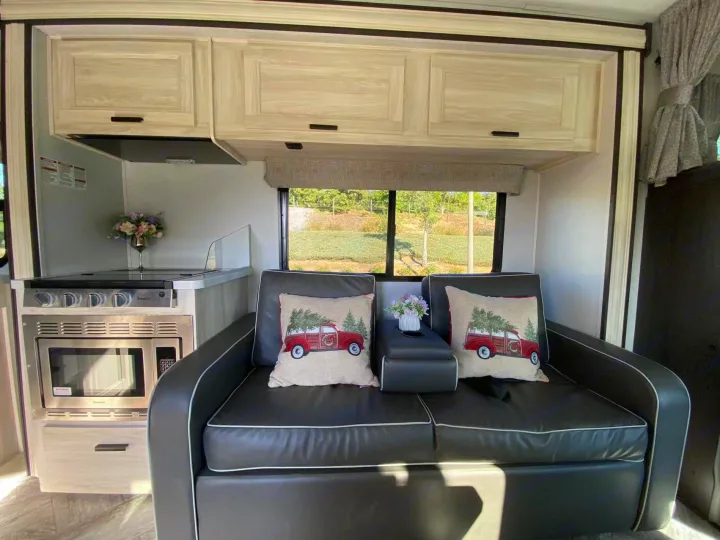 Inside a modern rv rental: compact kitchen with stovetop, microwave, comfy sofa, and scenic window view.. Forest River Sunseeker 2022