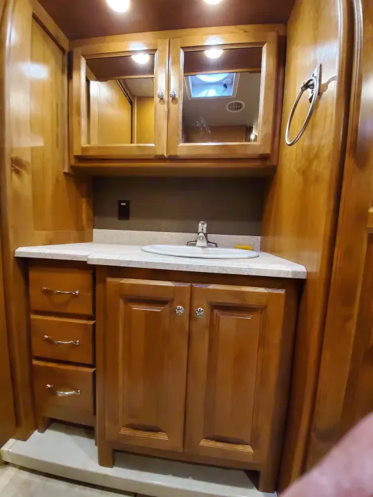 RV rental bathroom vanity: wooden cabinets, sink, mirror, and towel ring. Functional and compact design.. Tiffin Motorhomes Allegro Open Road 2016