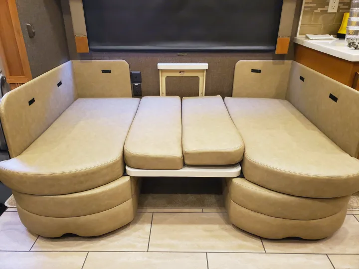 This RV rental features versatile beige dinette seating that converts into a comfortable bed, with power outlets visible.. Tiffin Motorhomes Allegro Open Road 2016