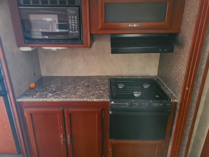 RV rental kitchen: Wood cabinets, black microwave, stove, range hood, and speckled countertop visible in this interior shot.. Keystone Passport Ultra-lite Grand Touring 2016