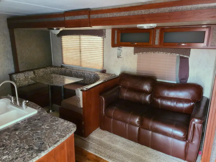 RV rental interior features a cozy dinette, comfortable brown sofa, and kitchen area with sink.. Keystone Passport Ultra-lite Grand Touring 2016
