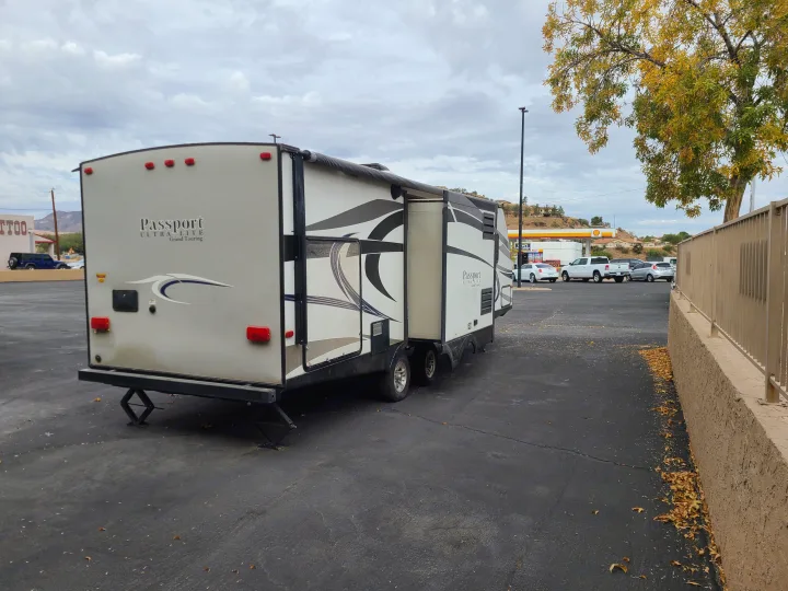 A parked Passport RV rental with slide-out extended in a paved lot, with a gas station and trees in the background.. Keystone Passport Ultra-lite Grand Touring 2016