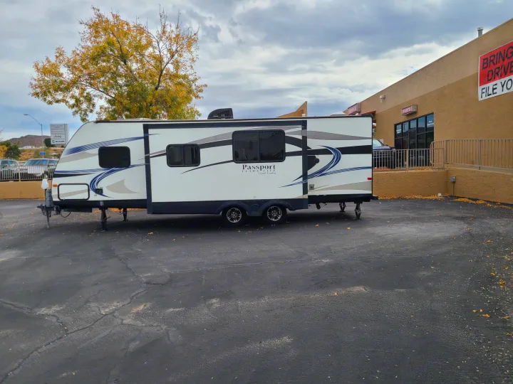 A white Passport travel trailer, ideal for an RV rental, is parked at a service center.. Keystone Passport Ultra-lite Grand Touring 2016