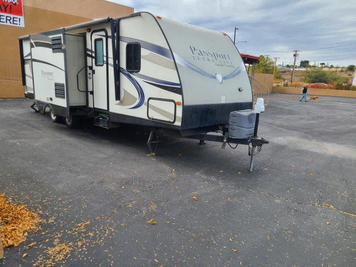 This gray and white Passport Ultra-Lite travel trailer, perfect for an RV rental, is parked with its slide-out extended.. Keystone Passport Ultra-lite Grand Touring 2016