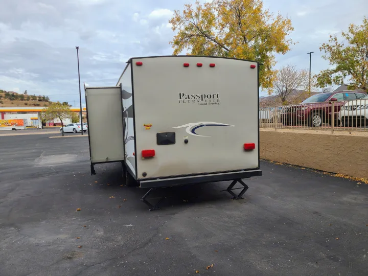 Rear of an RV rental, a Passport Ultra Lite travel trailer, parked with its side extended and stabilizers deployed.. Keystone Passport Ultra-lite Grand Touring 2016