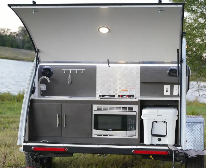 This compact RV rental features an open rear hatch revealing a fully equipped outdoor kitchen: sink, stove, microwave, and cooler.. nuCamp T@G 2021
