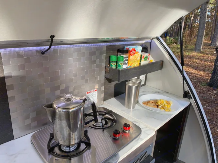 Teardrop RV rental kitchen galley with stove, coffee percolator, and breakfast, ready for outdoor meals.. nuCamp T@G 2021