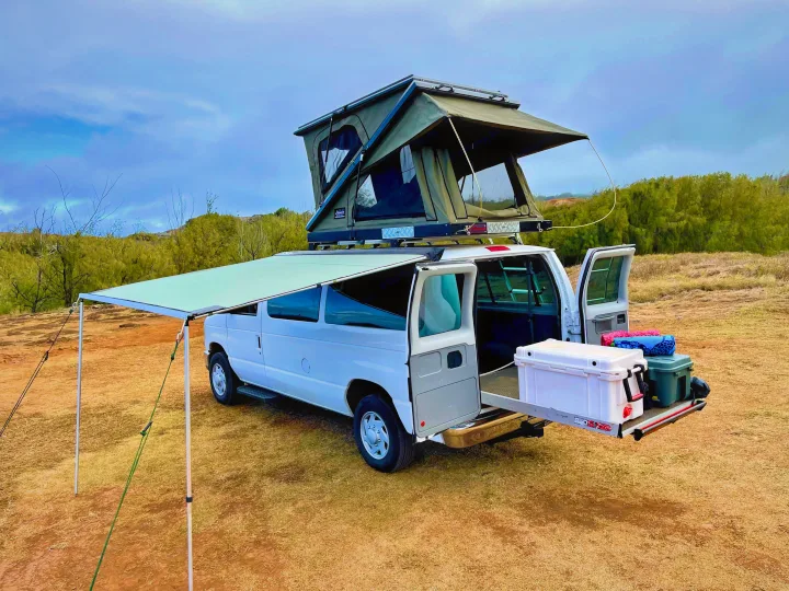 This RV rental van, with a deployed rooftop tent, side awning, and rear cooler pull-out, is ready for outdoor adventure.. Ford Econoline 2009