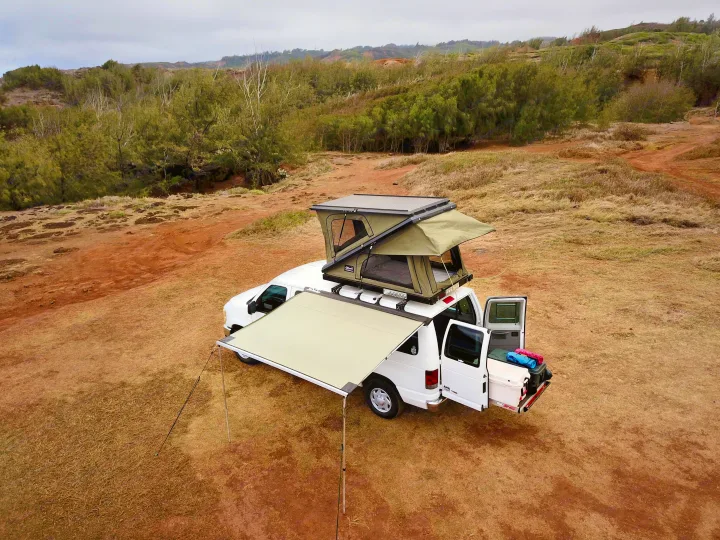Scenic RV rental van setup: white van with an open rooftop tent, extended awning, and rear loaded with camping gear.. Ford Econoline 2009
