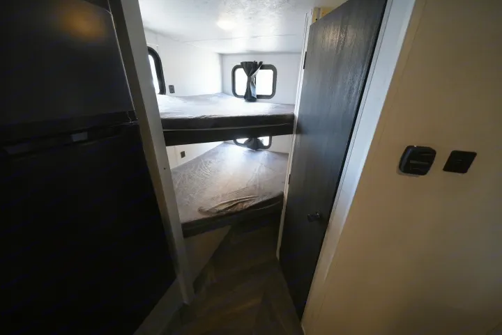 RV rental interior with stacked bunk beds, windows, and dark curtains. A functional and cozy sleeping area for travelers.. Forest River Wildwood FSX 2022