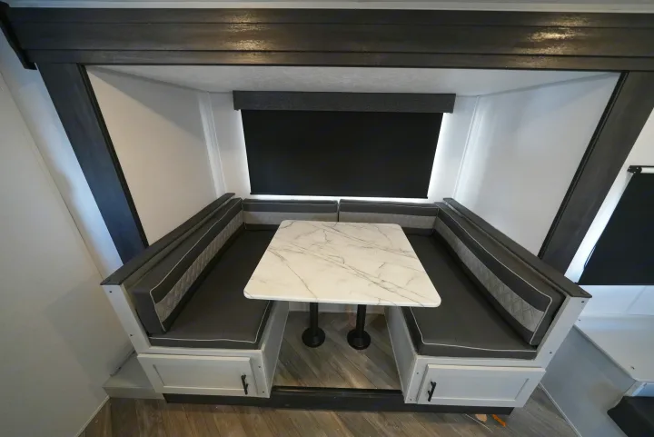 Modern RV rental dinette with dark grey booth seating, a white marble-patterned table, and dark wood accents.. Forest River Wildwood FSX 2022