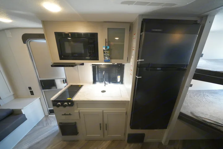 Explore this RV rental's sleek interior: a well-equipped kitchen with microwave, stove, sink, and refrigerator. Bunk beds also visible.. Forest River Wildwood FSX 2022
