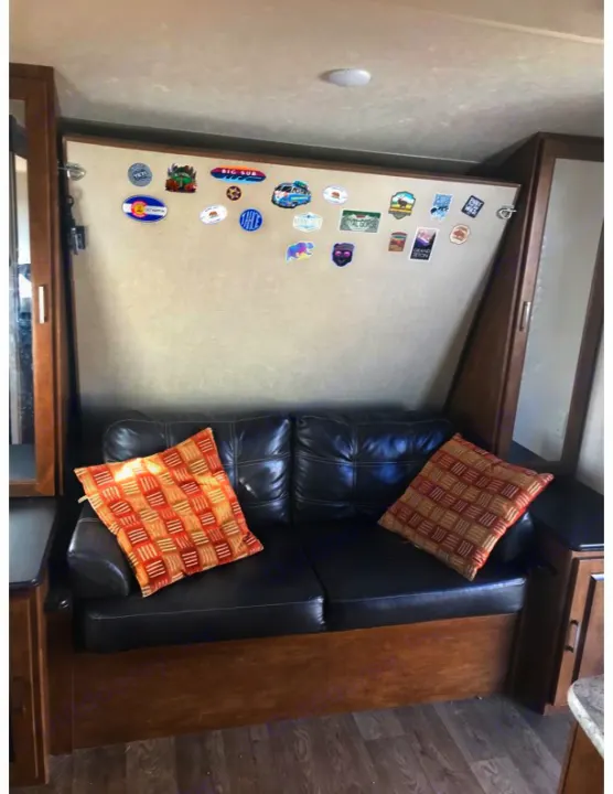 Explore the comfortable rv rental interior featuring a cozy black sofa and wall covered in memorable travel stickers.. Forest River Salem Cruise Lite 2018