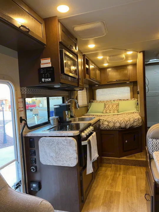 Step into this modern RV rental's inviting interior: a well-equipped kitchen and a comfortable bed await.. Thor Freedom Elite 2020