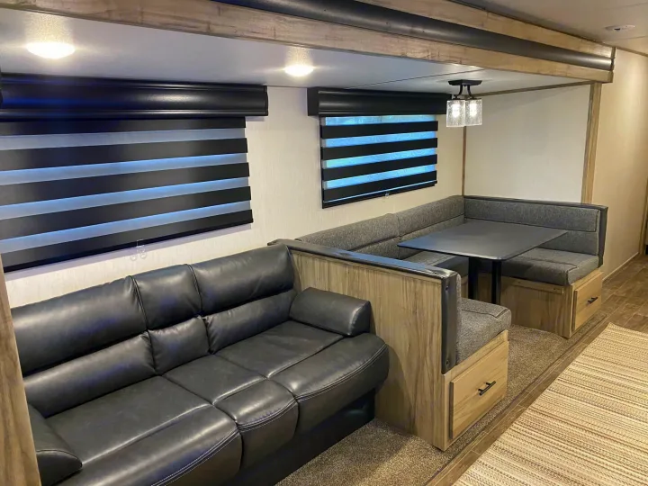 Spacious rv rental interior featuring a leather sofa, dinette, and modern window blinds.. Forest River Cherokee Alpha Wolf 2021