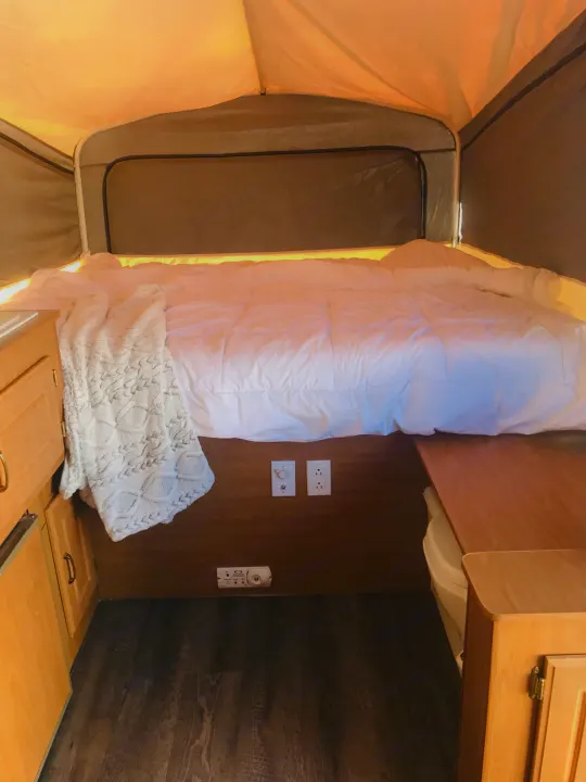 Cozy rv rental interior with a comfy bed, wood cabinetry, and amenities, perfect for compact travel.. Coleman Grand Tour Carmel 2003