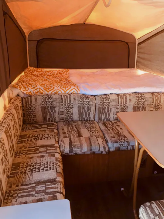Pop-up RV rental interior: features a cozy bed with patterned bedding, a U-shaped dinette, and a table.. Coleman Grand Tour Carmel 2003
