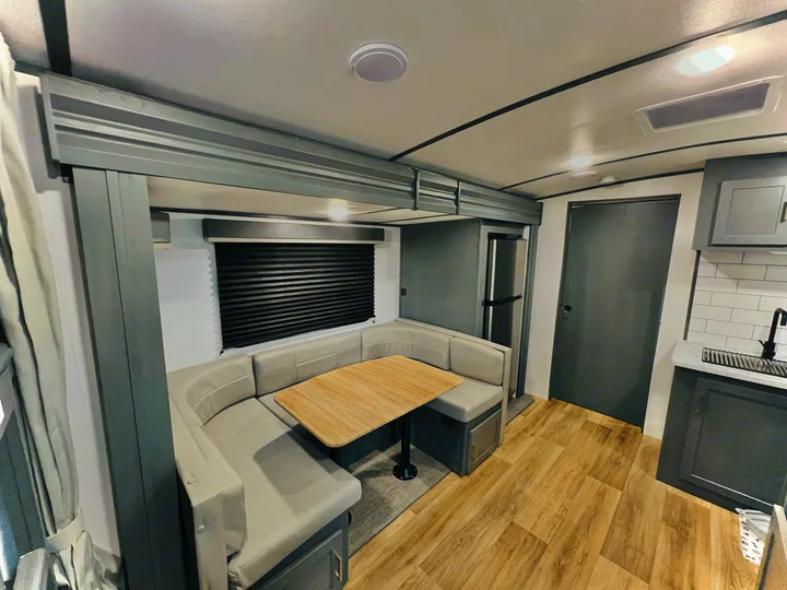 Spacious RV rental interior: modern grey dinette, wood table, light wood floors, and kitchen.. Keystone Bullet 250BHS 2022