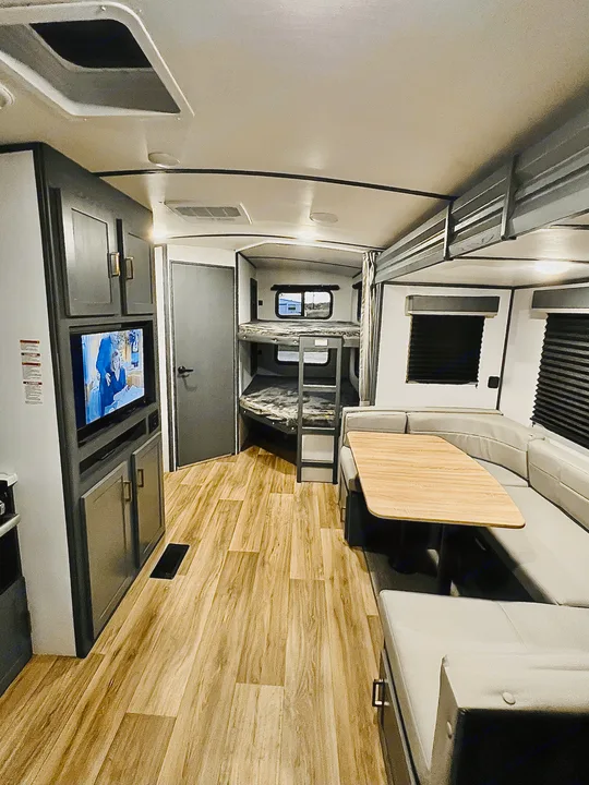 Spacious RV rental interior: a bright living area with a U-shaped dinette, TV, and bunk beds, featuring wood-look flooring.. Keystone Bullet 250BHS 2022