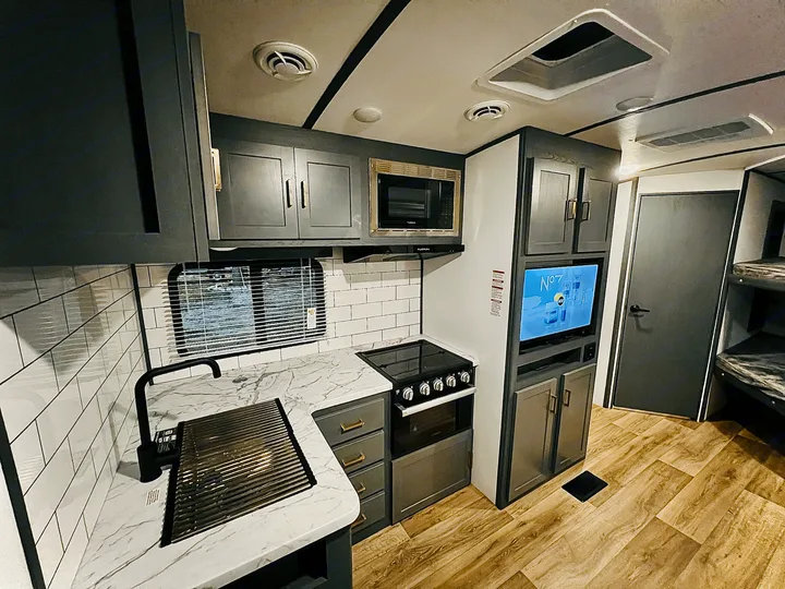 Spacious RV rental interior: modern kitchen with dark cabinets, white counters, stove, sink, and adjacent TV/bunk area.. Keystone Bullet 250BHS 2022
