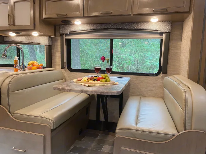 Inside a comfortable RV rental: dining booth with charcuterie, wine, and a scenic forest view.. Thor Magnitude GA 2022